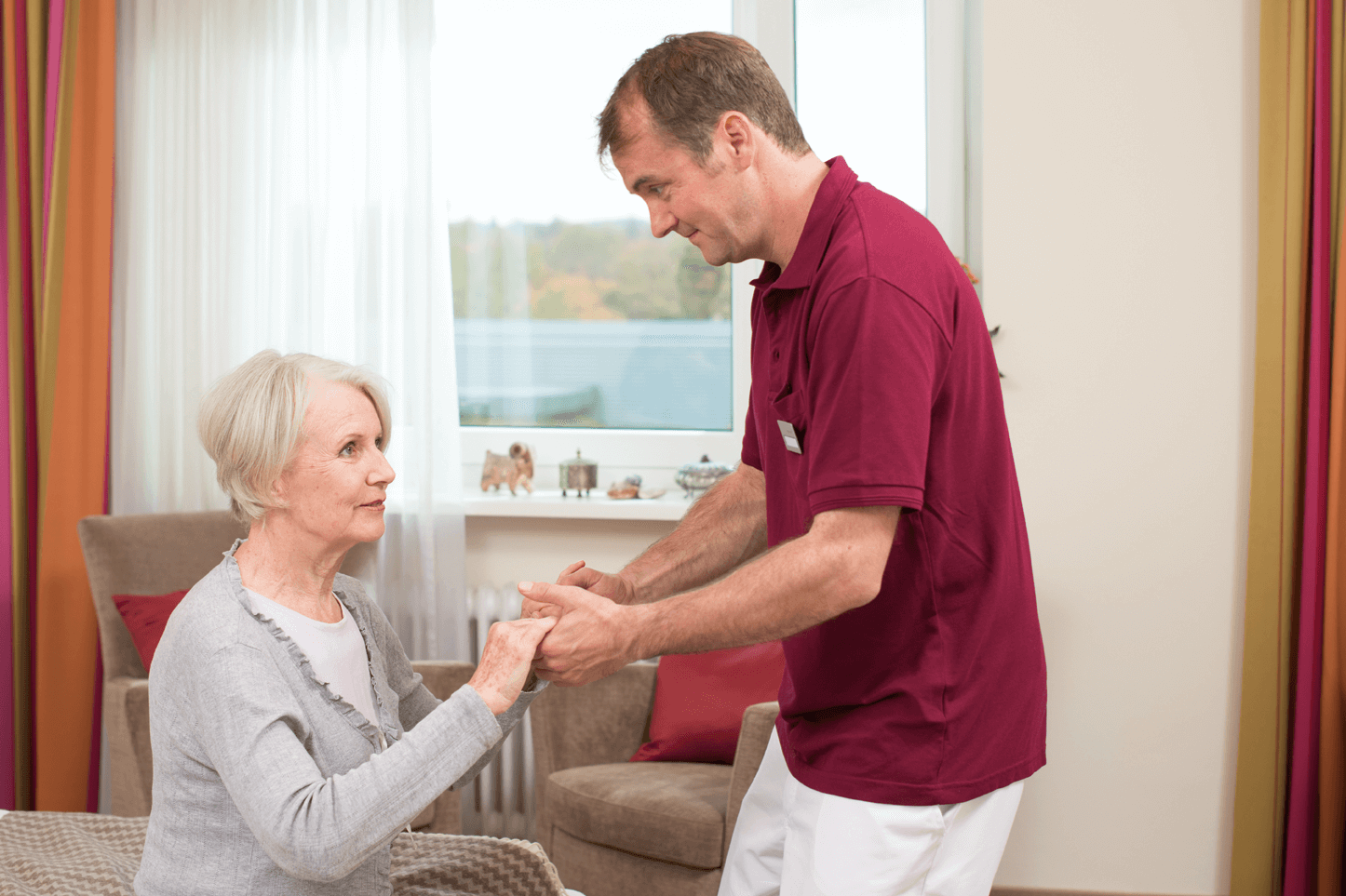 Tagesbetreuung für Menschen mit Demenz Pfleger hilft älterer Dame beim Aufstehen
