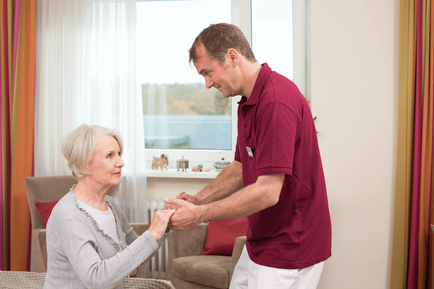 Tagesbetreuung für Menschen mit Demenz Pfleger hilft älterer Dame beim Aufstehen