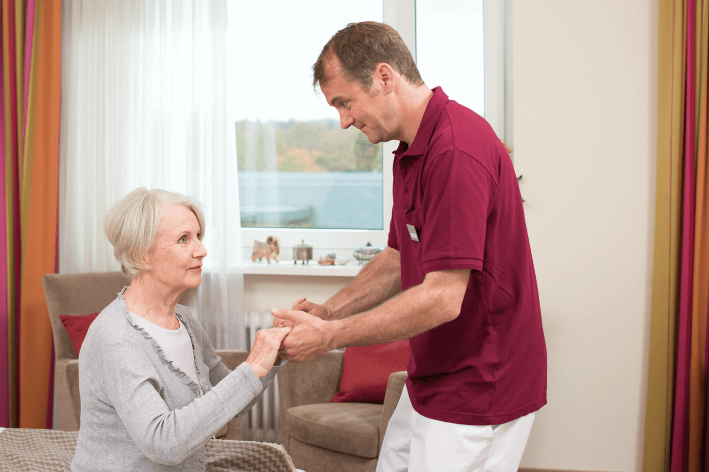 Tagesbetreuung für Menschen mit Demenz Pfleger hilft älterer Dame beim Aufstehen