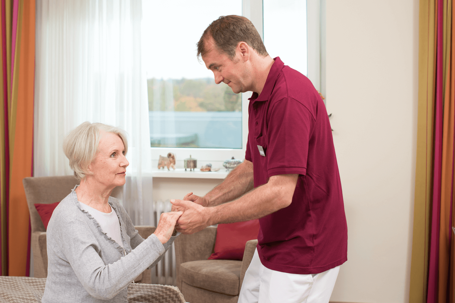 Tagesbetreuung für Menschen mit Demenz Pfleger hilft älterer Dame beim Aufstehen