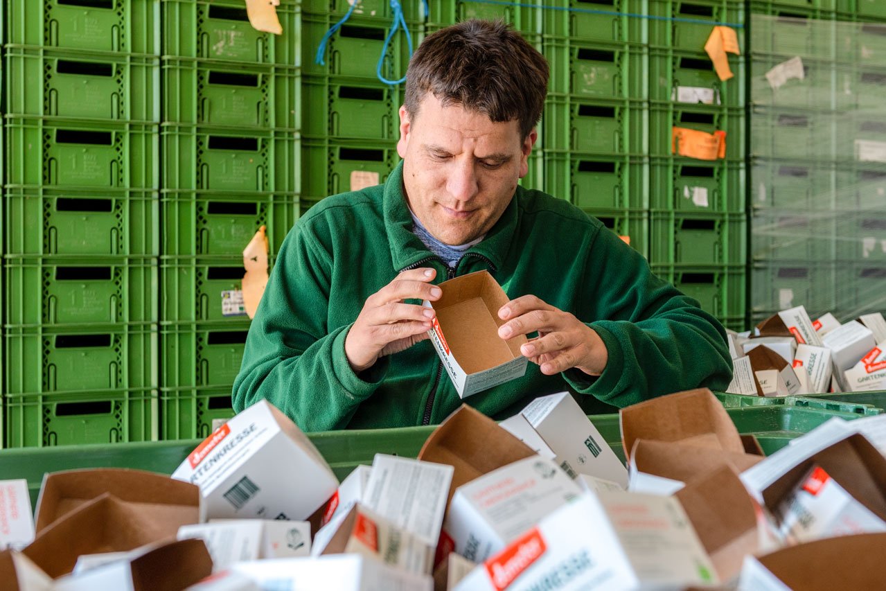 Kresseverpackung Ein Klient der Augustinum Gärtnerei Hollern faltet Kresseverpackungen
