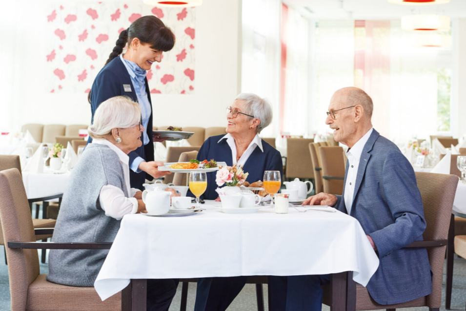 Augustinum Seniorenresidenz Braunschweig Drei Senior*innen werden beim Frühstück von einer Mitarbeiterin des Augustinum bedient
