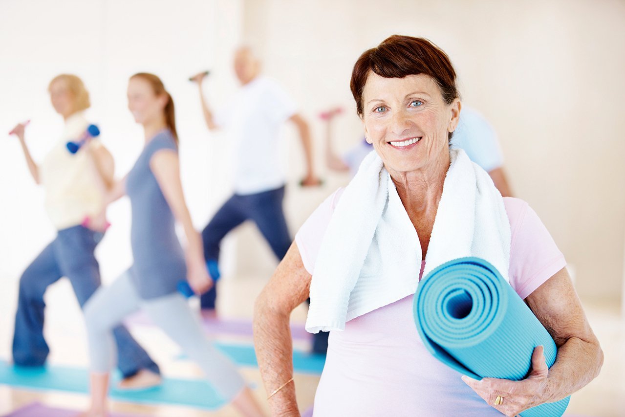 Aktiv sein Eine lächelnde Seniorin mit einer Yogamatte in der Hand