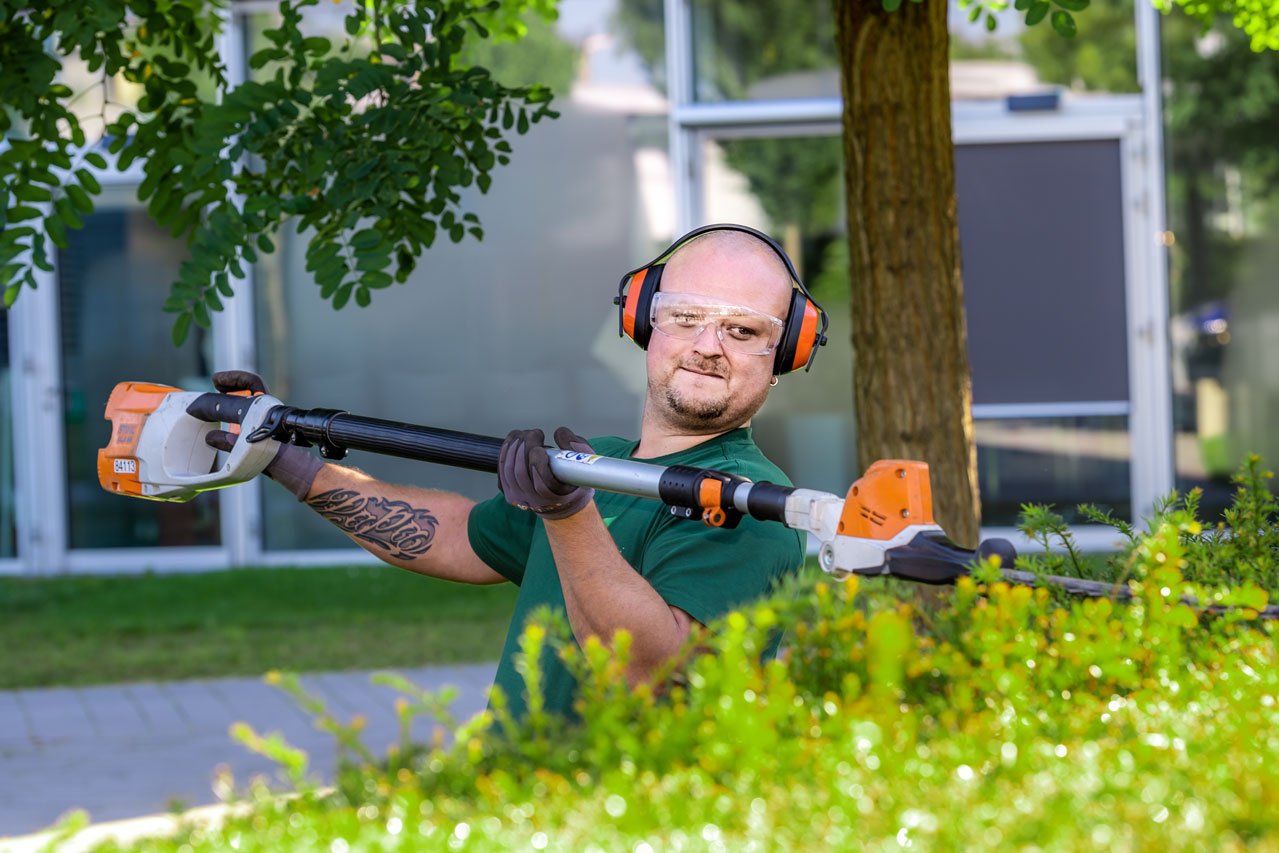 Heckenschneiden Ein Klient der Augustinum Gärtnerei Hollern schneidet mit einer akkubetriebenen Teleskopheckenschere die Hecke