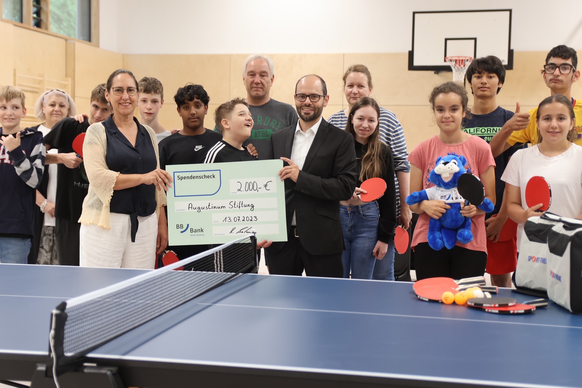 Augustinum Spenden Erfolge Tischtennis Ein Gruppenfoto mit Schüler*innen der Otto-Steiner-Schule hinter einer Tischtennisplatte mit einem Spendenscheck für die Tischtennisausstattung der Schule